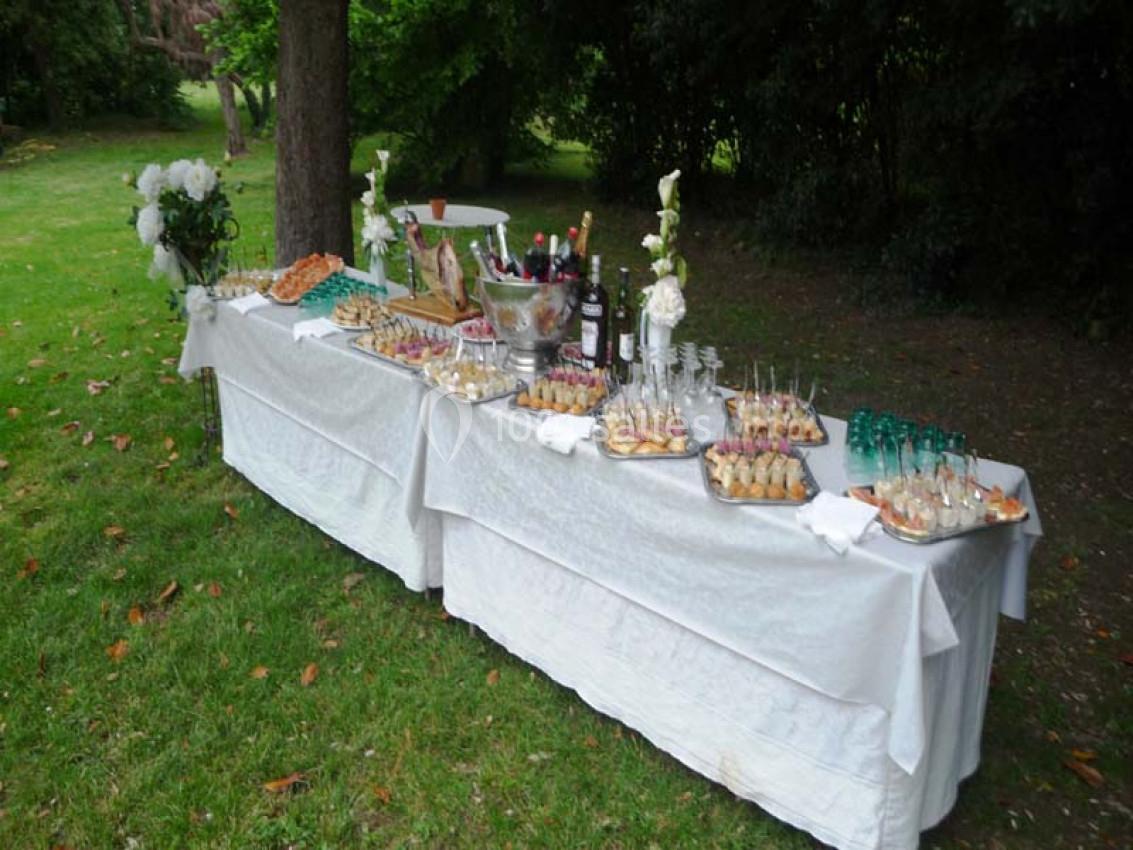 Table dressée en extérieur avec des plats variés, des boissons et des décorations florales sur une nappe blanche.