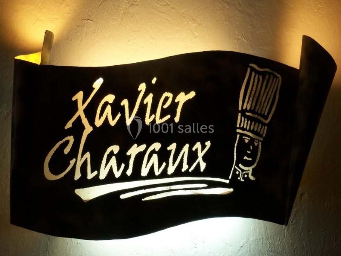 Enseigne en métal noir avec le texte ’Xavier Charaux’ et un dessin de toque de chef éclairés par une lumière chaude.