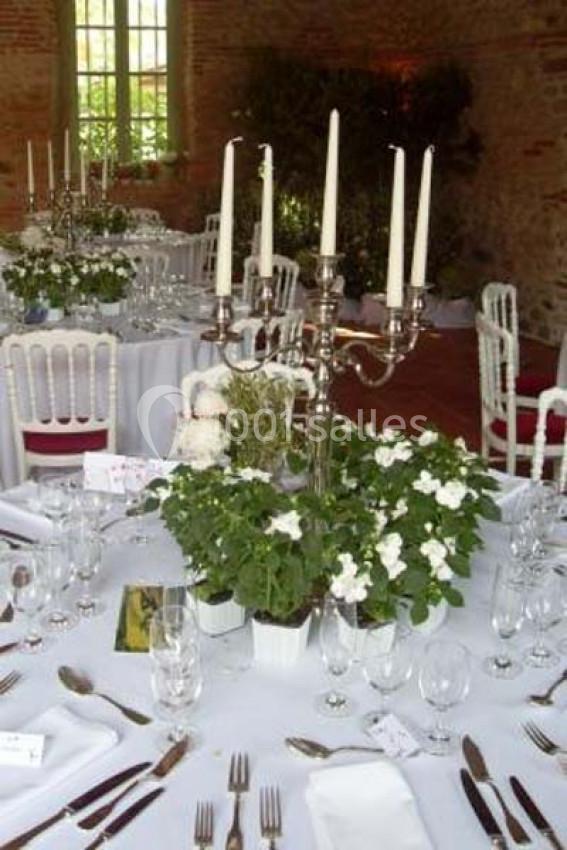 Tables de réception décorées avec des chandeliers, des fleurs blanches et une vaisselle élégante dans une salle lumineuse.
