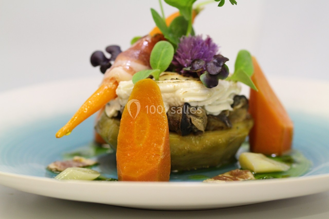 Assiette gastronomique composée de légumes colorés, fromage frais et herbes, présentée sur un fond bleu.