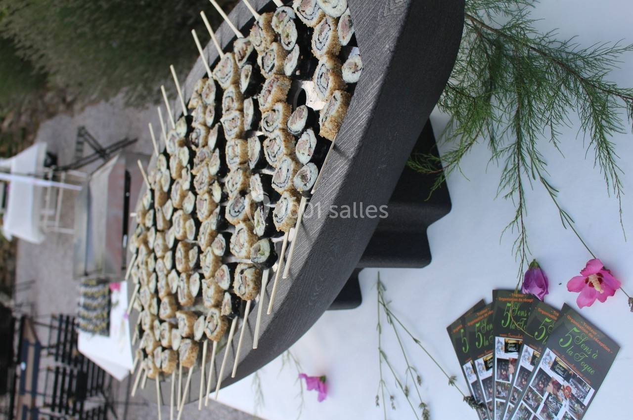 Plateau en forme de bateau rempli de brochettes de sushis, entouré de fleurs et de prospectus sur une table blanche.