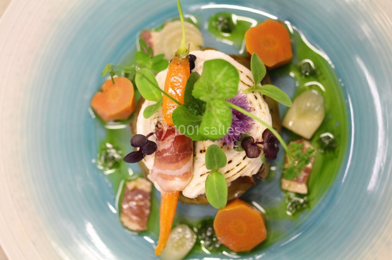 Assiette gastronomique colorée avec légumes, viande, herbes fraîches et sauce verte, présentée sur une assiette bleue.