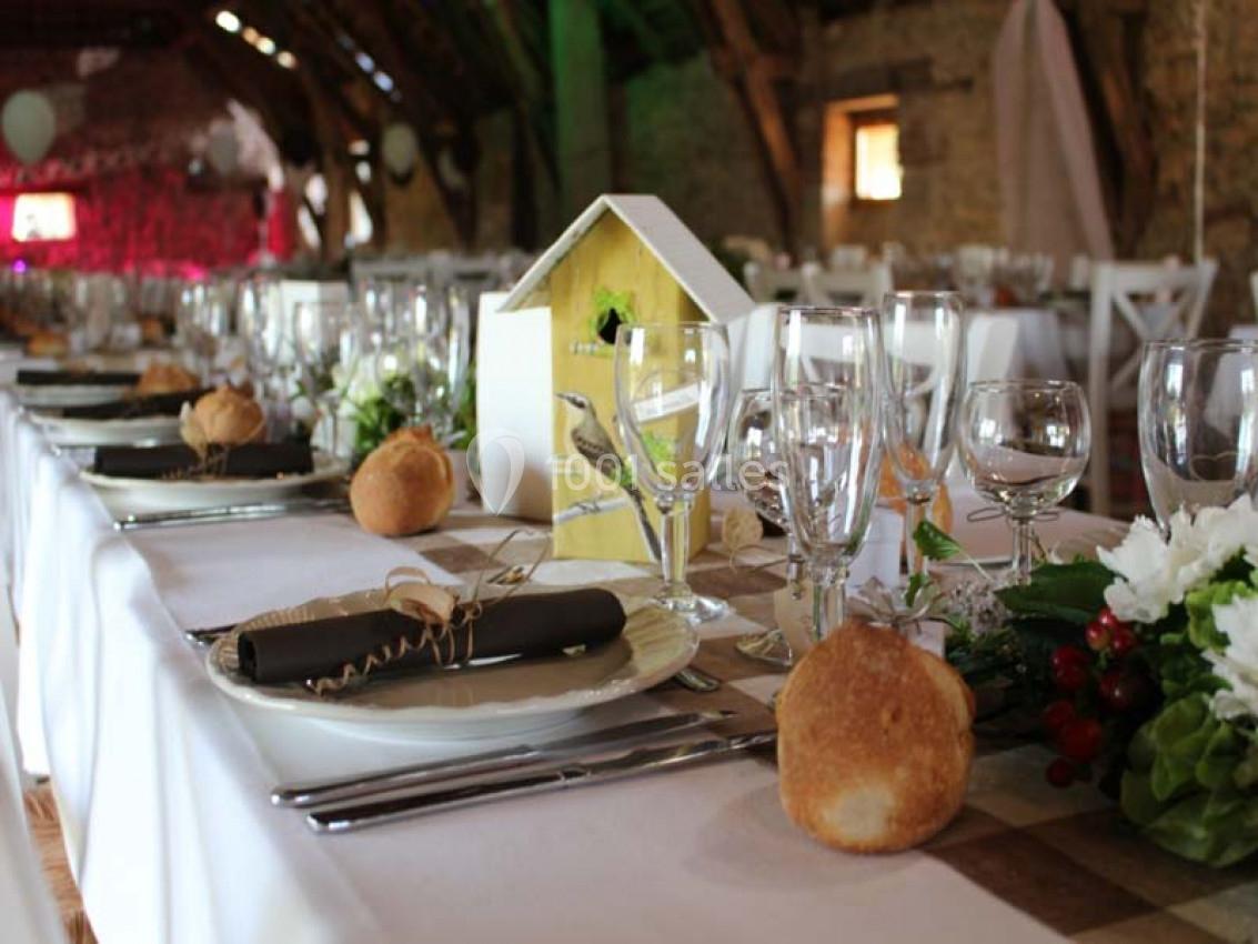 Table dressée pour un repas festif dans une salle rustique, avec décorations florales et pain individuel.