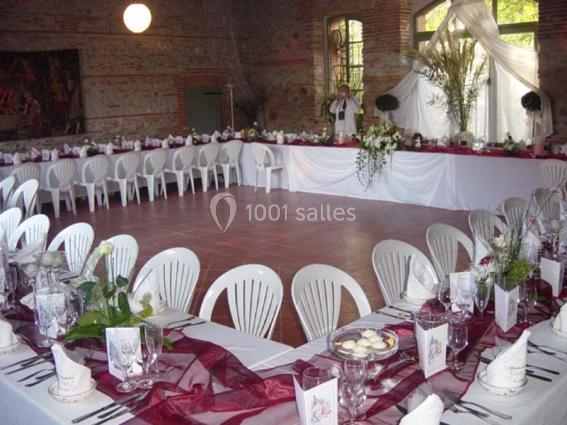 Salle de réception décorée pour un événement, avec longues tables dressées, nappes blanches et ornements floraux.