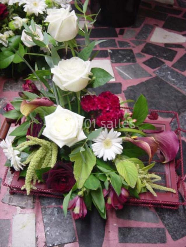 Arrangement floral avec roses blanches, fleurs rouges et feuillage vert, posé sur un cadre rouge sur un sol en mosaïque.