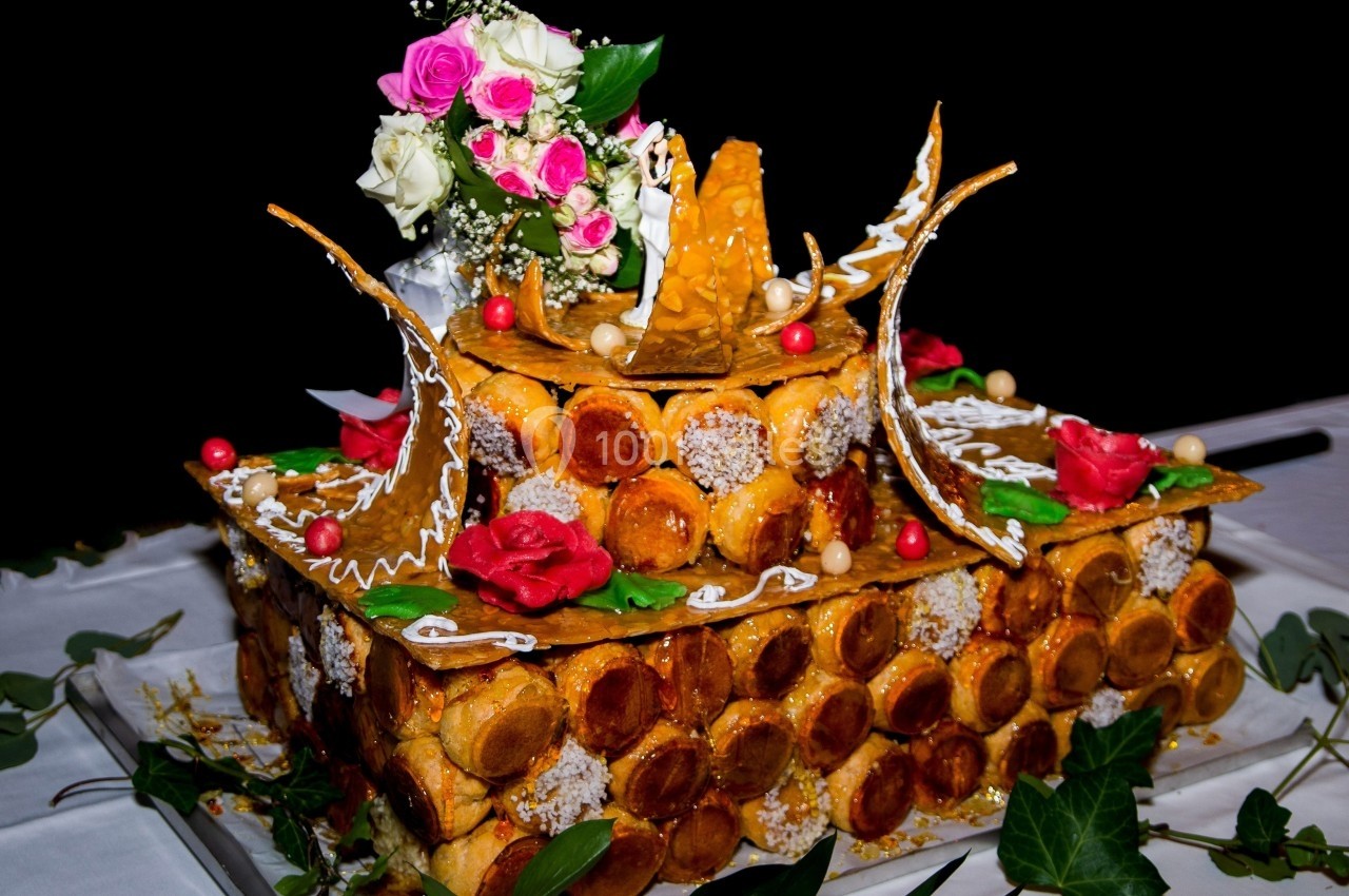 Pièce montée en choux décorée de roses, feuilles vertes et éléments en caramel sur une table blanche.