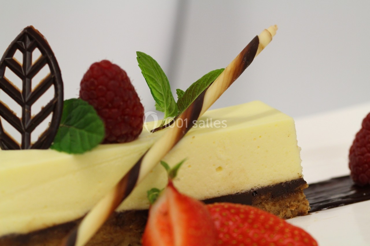 Part de gâteau au citron surmontée de framboises, feuilles de menthe, décor en chocolat et fraises en avant-plan.