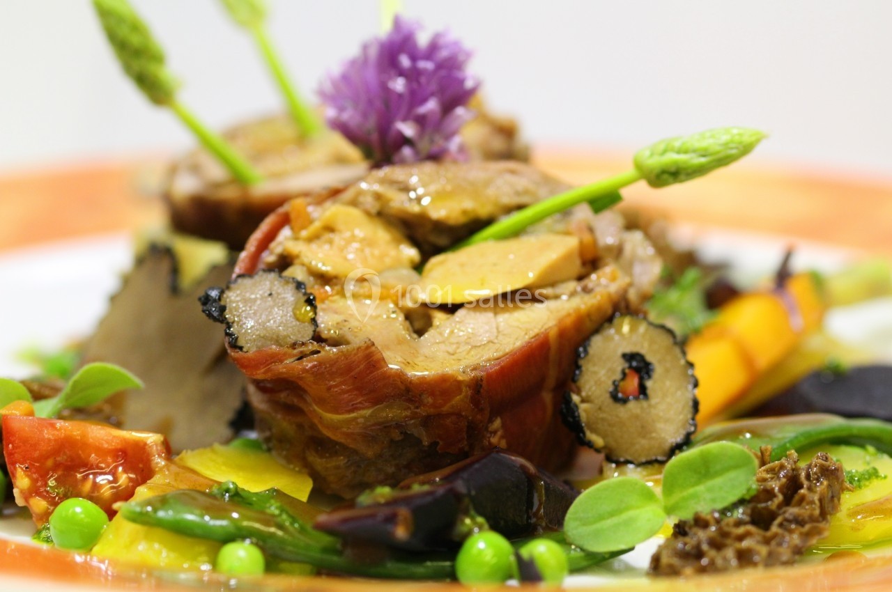 Plat gastronomique composé de viande enroulée, légumes colorés, truffes et asperges, présenté avec soin.