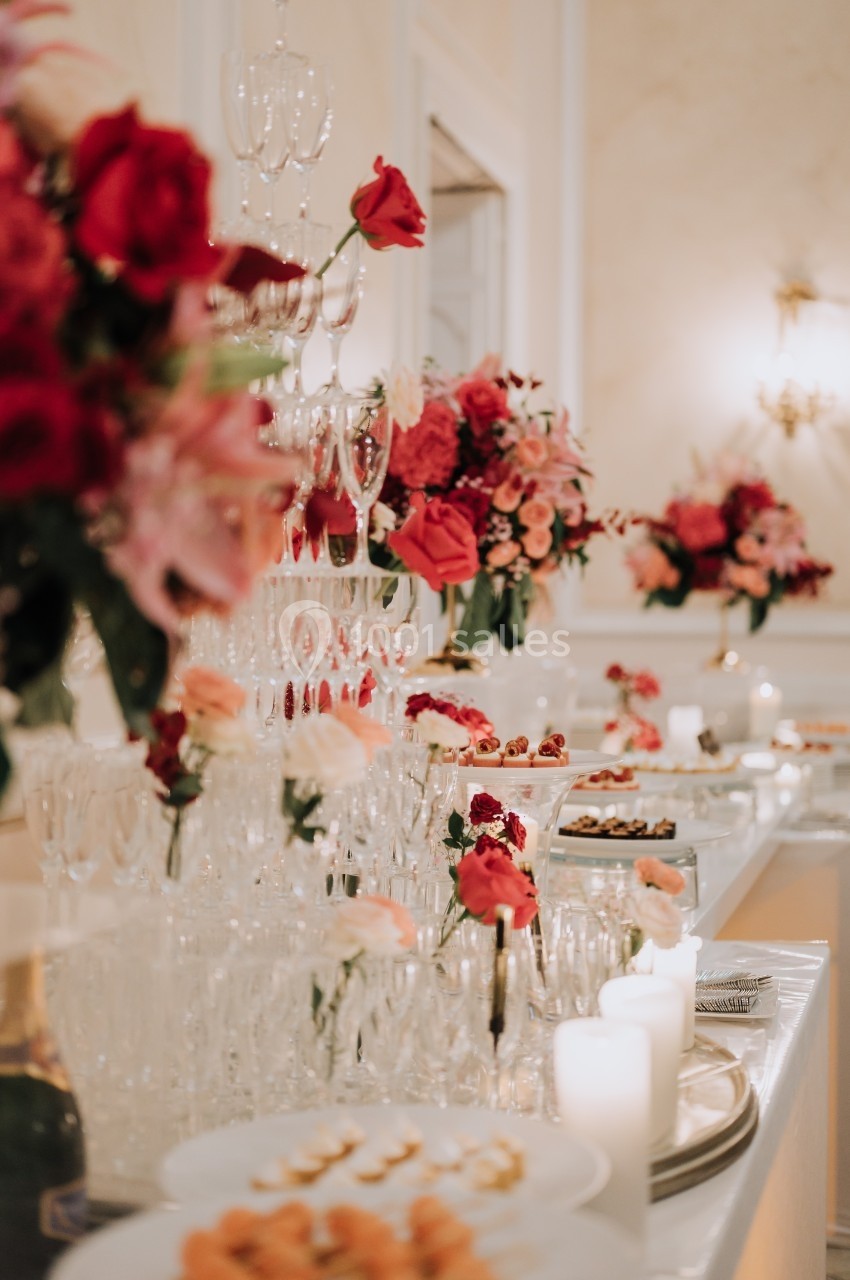 Table décorée avec des fleurs rouges et roses, des chandelles blanches et des plats d'apéritifs élégamment disposés.