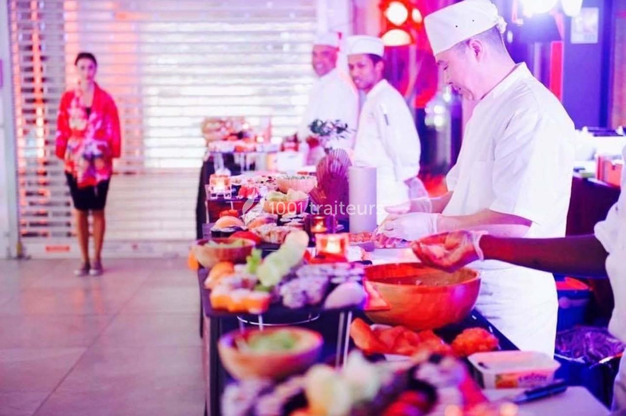 Des chefs préparent des plats sur un buffet garni de mets variés dans un espace lumineux et animé.
