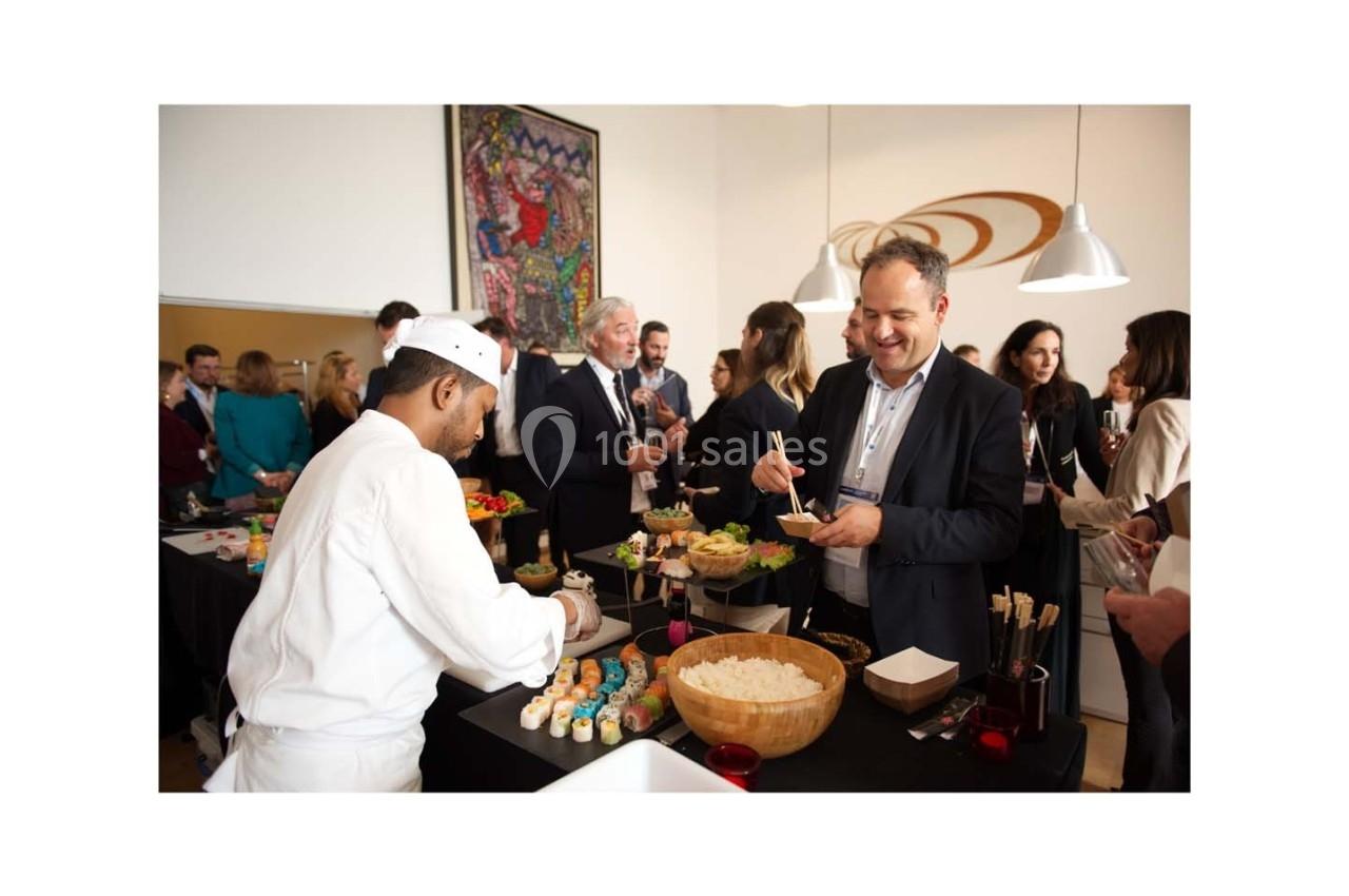 Un chef prépare des sushis pour des invités lors d'un événement professionnel dans une salle lumineuse.