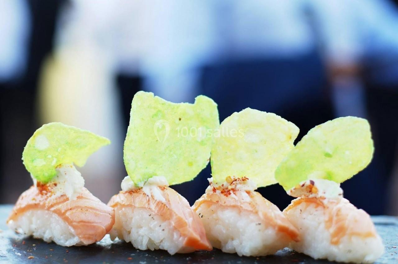 Sushis au saumon garnis de chips vertes, alignés sur une surface sombre avec un arrière-plan flou.
