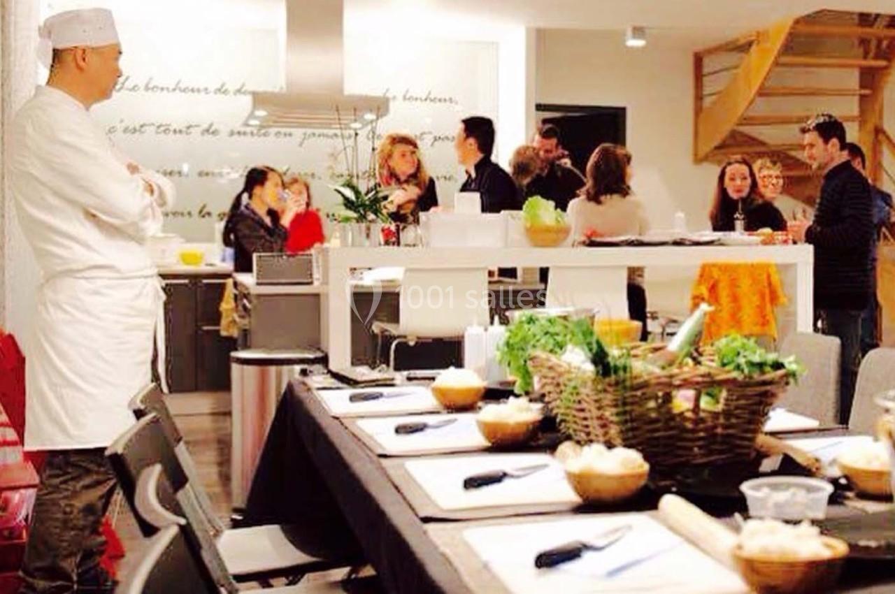 Un chef observe un groupe de personnes discutant autour d'une table dans une cuisine conviviale.