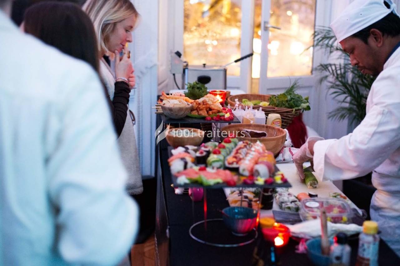 Un chef prépare des sushis sur un buffet tandis que des convives observent la présentation des plats.