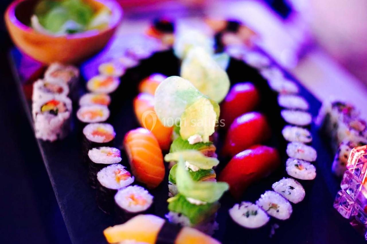 Plateau de sushis variés avec makis, sashimis et chips, présenté sur une table éclairée par une lumière colorée.