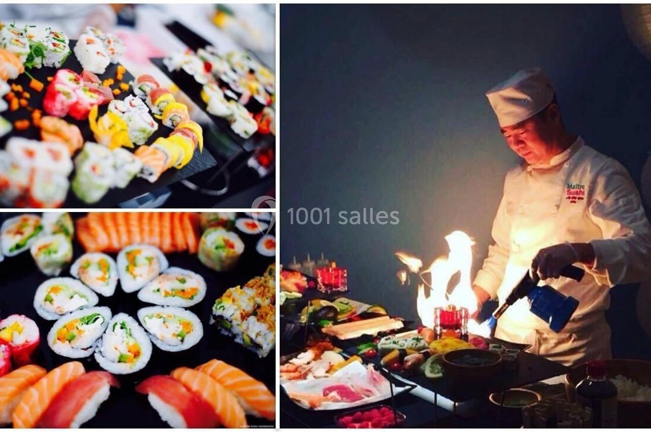 Un chef prépare des sushis variés avec un chalumeau, entouré de plateaux garnis de sushi et makis colorés.