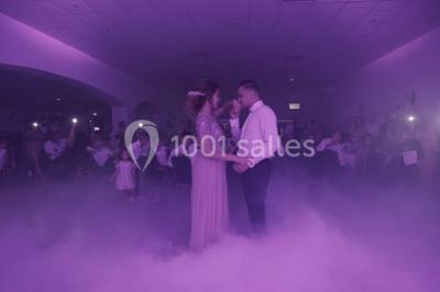 Table dressée avec nappes blanches, verres et couverts, vue sur une terrasse avec piscine et chaises en arrière-plan.