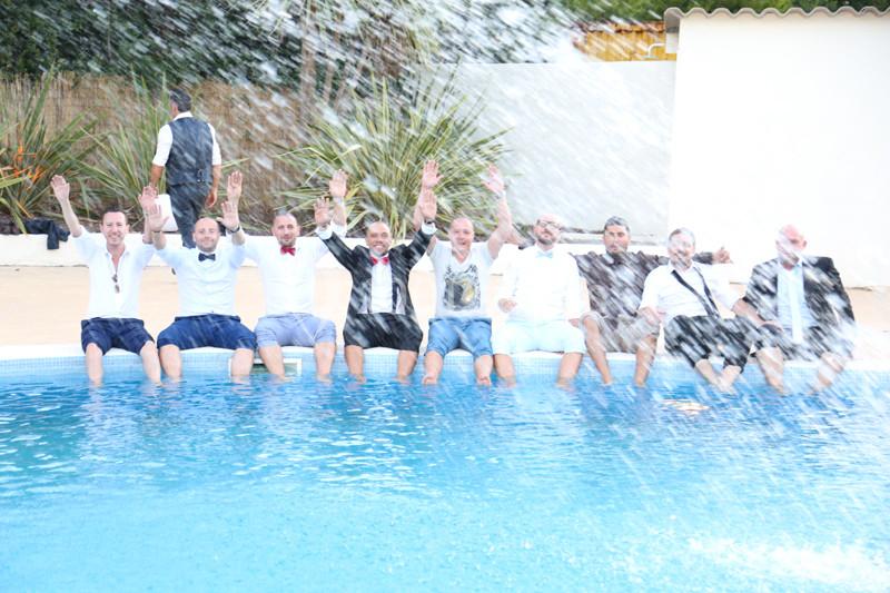 Des hommes assis au bord d'une piscine, levant les bras, avec des éclaboussures d'eau au premier plan.