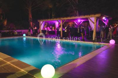 Table dressée avec nappes blanches, verres et couverts, vue sur une terrasse avec piscine et chaises en arrière-plan.
