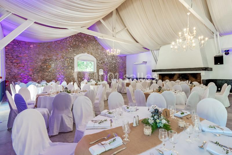Salle de réception décorée avec des tables rondes dressées, des chaises blanches et un éclairage tamisé.