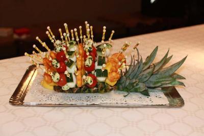 Plateau de brochettes apéritives colorées disposées sur une base d'ananas, présenté sur une nappe blanche.