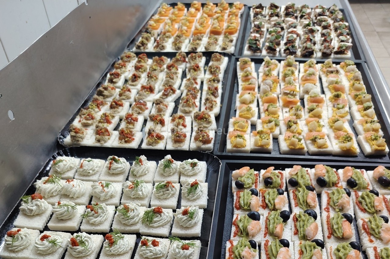 Plateaux de canapés variés garnis de légumes, crevettes, saumon et autres ingrédients, disposés sur une table.