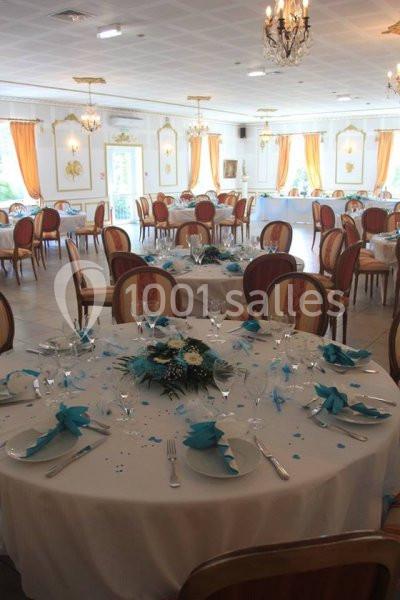 Salle de réception élégante avec tables rondes dressées, nappes blanches, décorations bleues et chaises en bois.