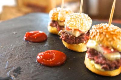 Mini burgers au bœuf garnis de fromage sur un plateau ardoise, accompagnés de petites portions de sauce ketchup.