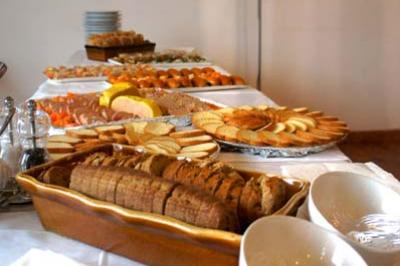Buffet avec pain tranché, biscuits, fruits et plats variés disposés sur une table blanche éclairée par une lampe.