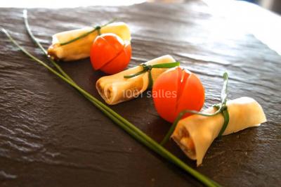 Une cheffe en tenue blanche prépare des plats sur un buffet lors d'un événement avec des convives en arrière-plan.