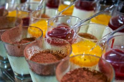 Une cheffe en tenue blanche prépare des plats sur un buffet lors d'un événement avec des convives en arrière-plan.