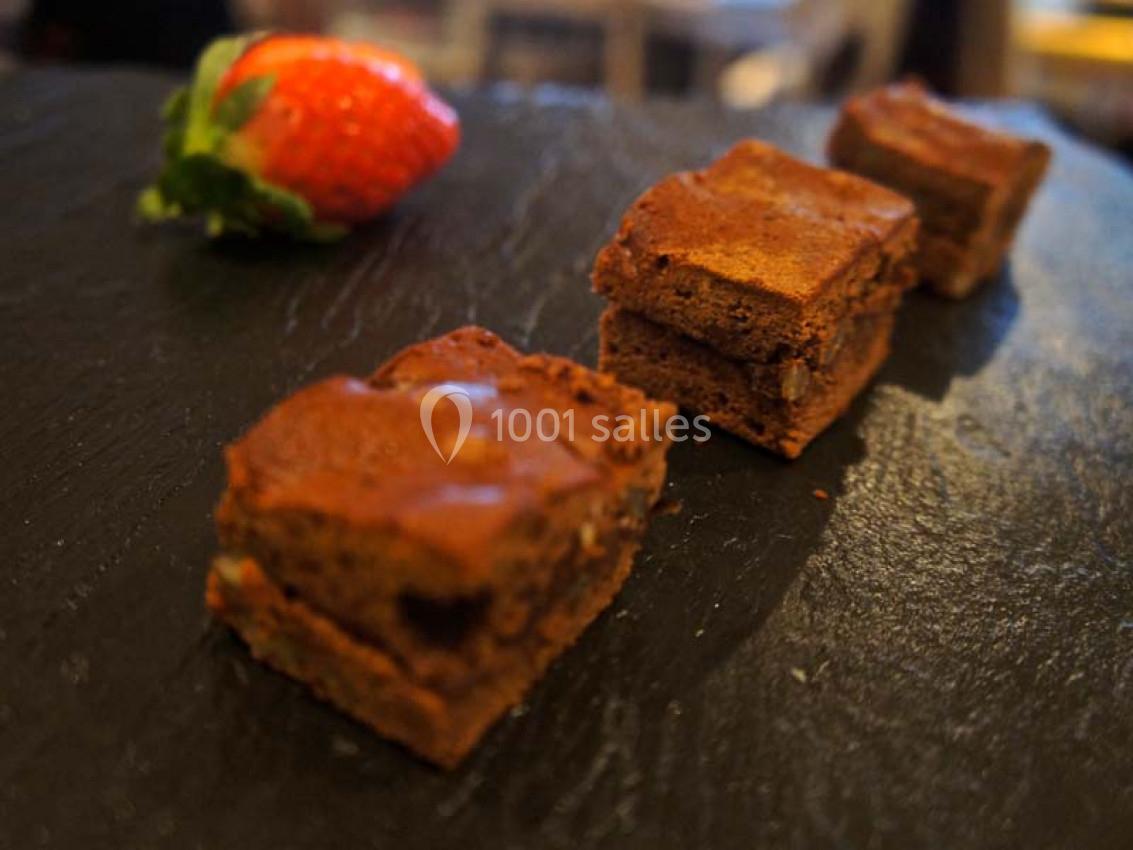 Carrés de brownie au chocolat disposés sur une ardoise noire avec une fraise en arrière-plan.