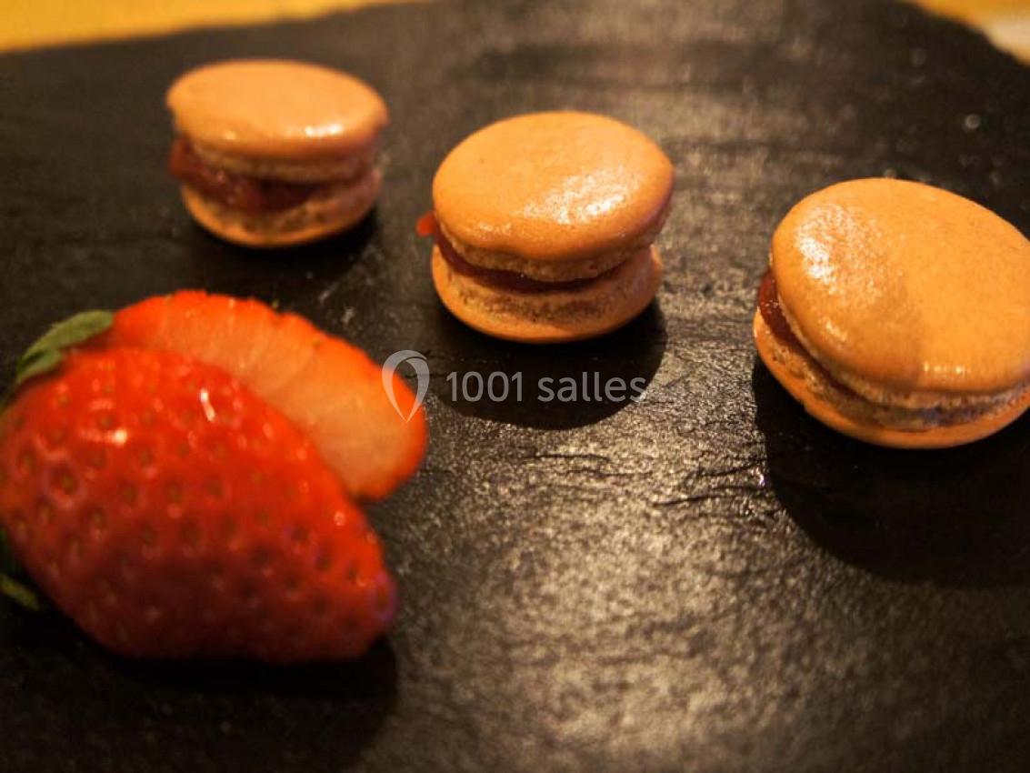 Trois macarons orange et une fraise tranchée disposés sur une ardoise noire.