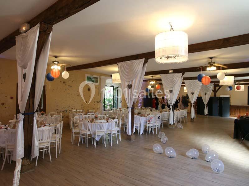Salle de réception décorée avec des tables dressées, des ballons suspendus et des rideaux blancs.