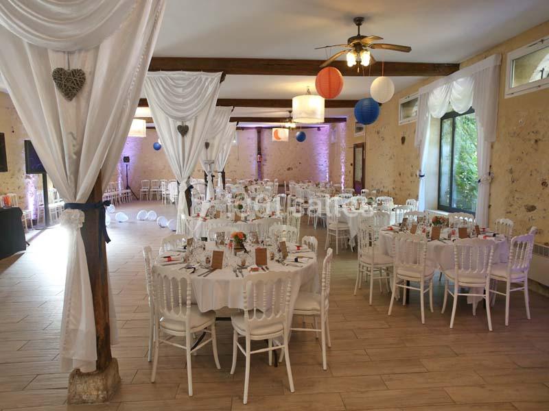 Salle de réception décorée avec des tables rondes, nappes blanches, chaises assorties et lanternes suspendues.