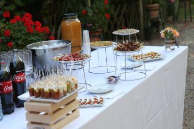 Table dressée en extérieur avec nappes blanches, boissons et verres, entourée de buissons fleuris d'hortensias.