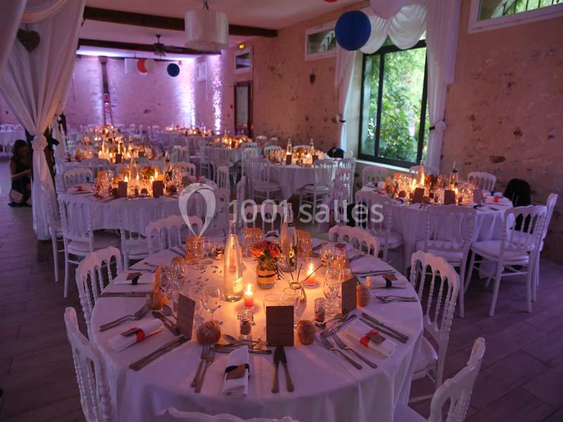 Salle de réception décorée avec des tables rondes dressées, éclairage tamisé et murs en pierre apparente.