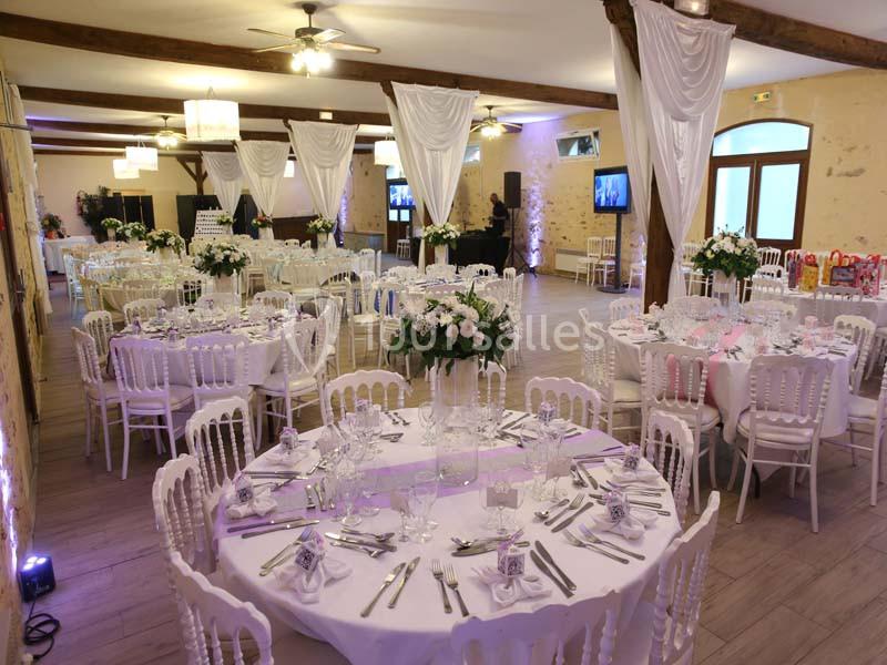 Salle de réception décorée avec des tables rondes dressées, des chaises blanches et des rideaux blancs suspendus.