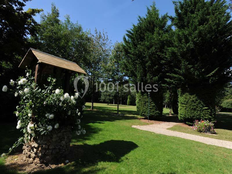 Un puits fleuri entouré de pelouse et d'arbres dans un jardin ensoleillé.
