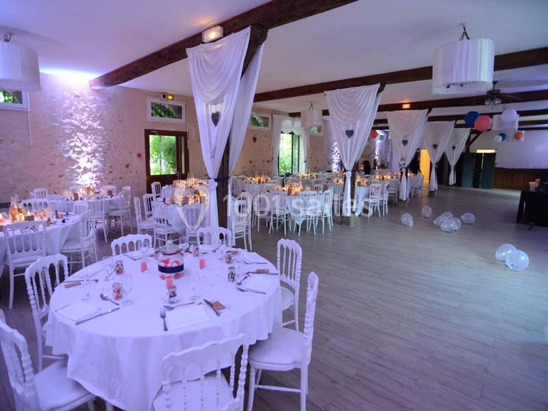 Salle de réception décorée avec des tables rondes, chaises blanches, rideaux suspendus et ballons au sol.