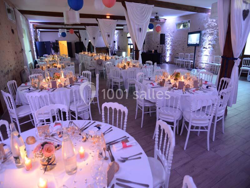 Salle de réception décorée avec des tables rondes dressées, nappes blanches, bougies et éclairage tamisé.