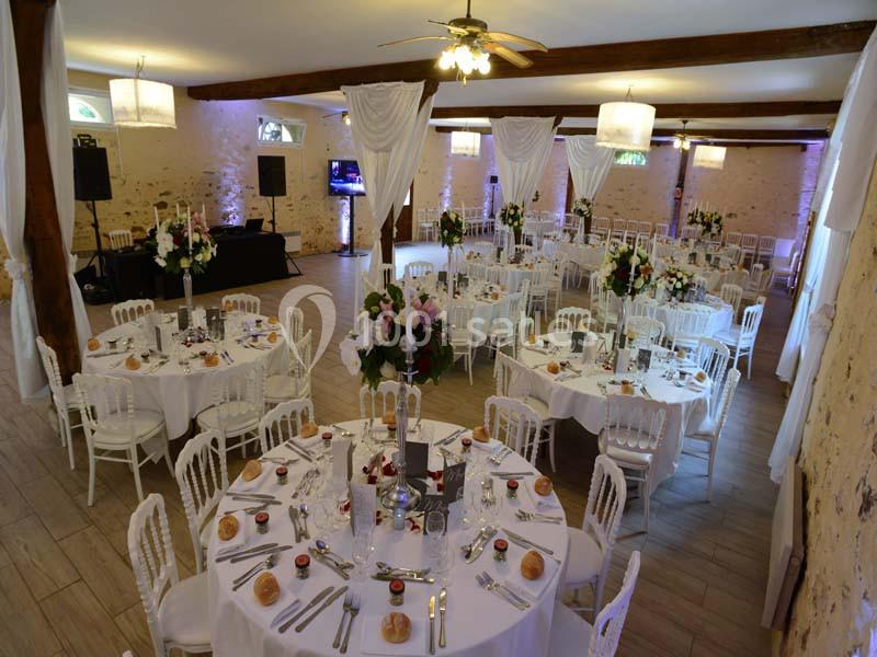 Salle de réception décorée avec des tables rondes dressées, chaises blanches et arrangements floraux élégants.