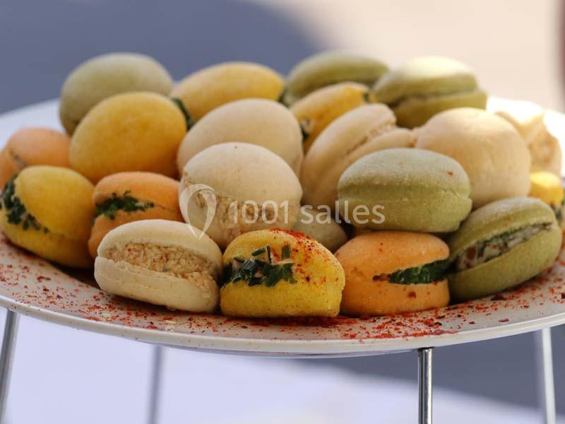 Assortiment de petits macarons salés garnis d'herbes et d'épices, présentés sur un plateau blanc.