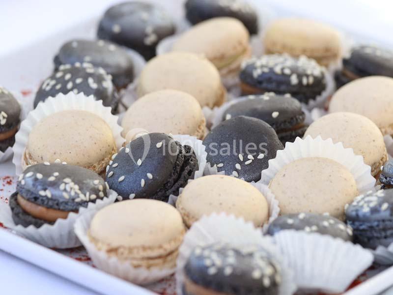 Assortiment de macarons noirs et beiges garnis, certains décorés de graines de sésame, présentés sur un plateau.