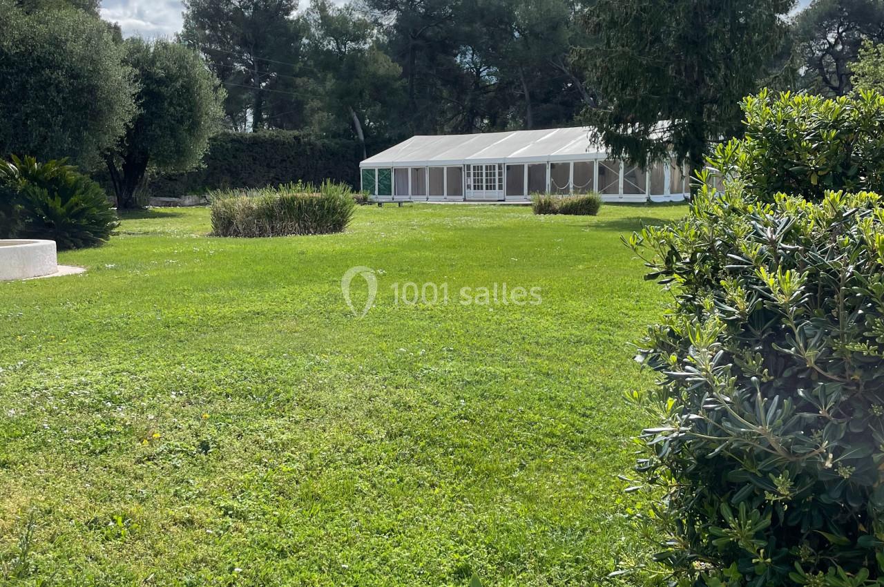 Pelouse verdoyante avec une grande tente blanche en arrière-plan, entourée d'arbres et de buissons.