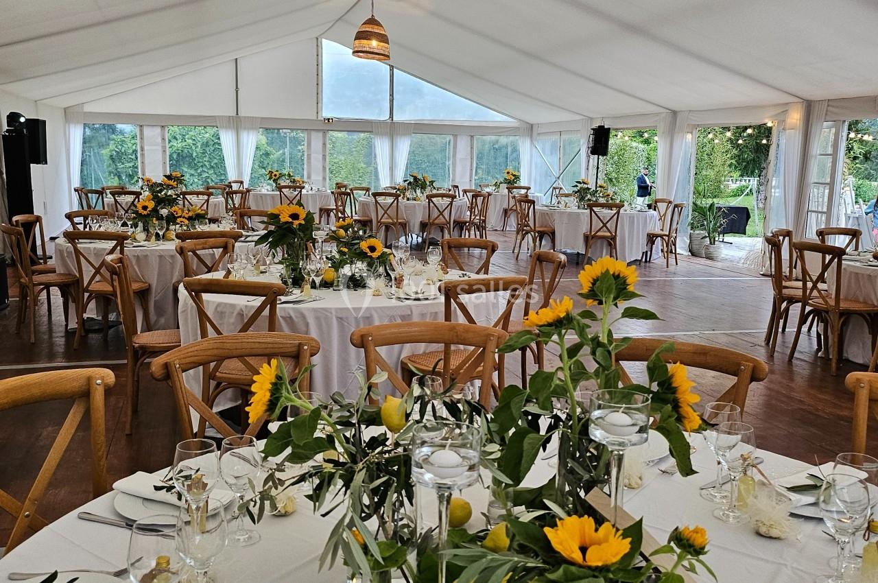 Salle de réception lumineuse sous une tente, décorée avec des tables ornées de tournesols et de citrons.