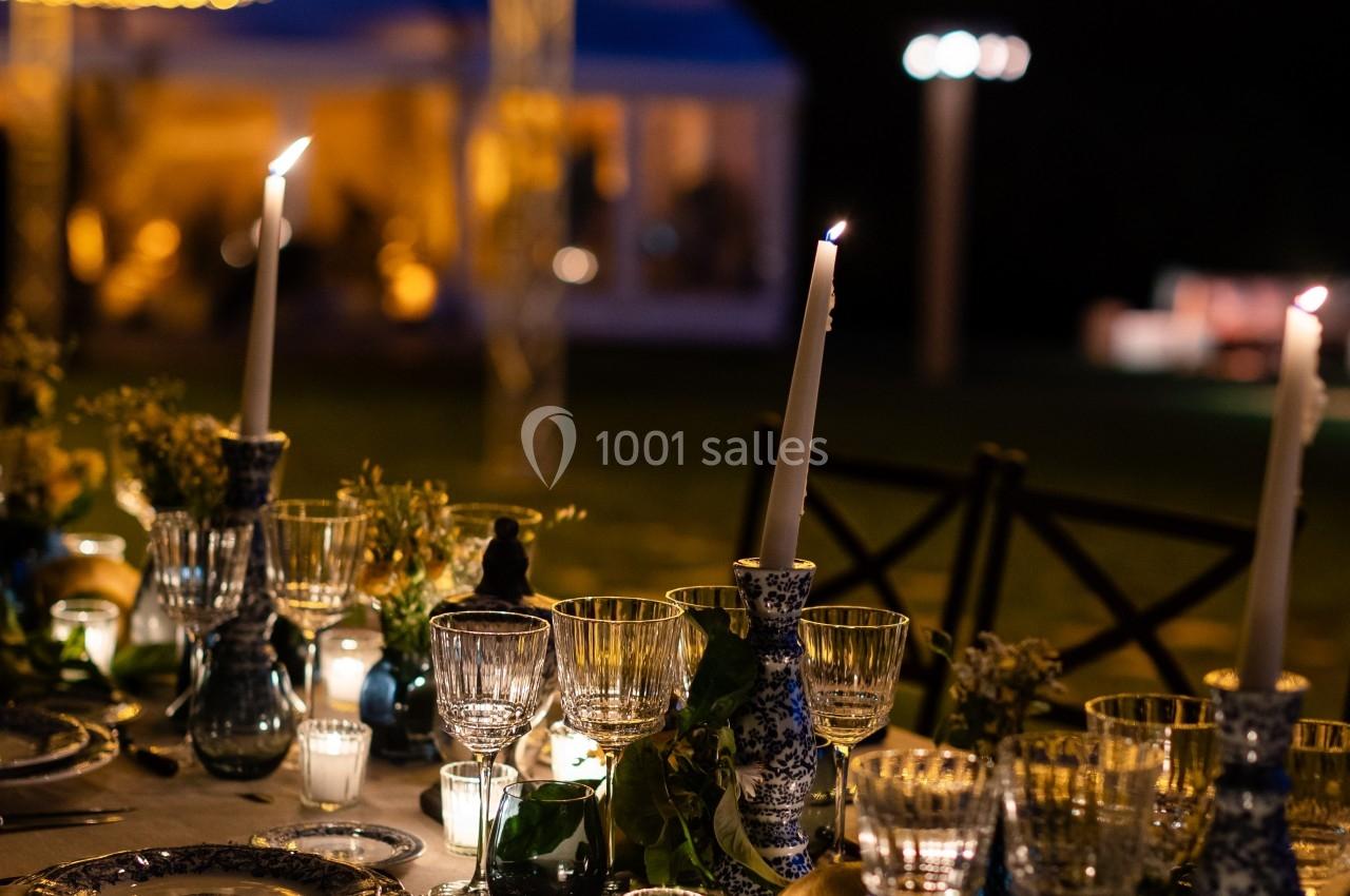 Table élégamment dressée avec chandeliers, verres et décorations sous un plafond illuminé de guirlandes lumineuses.