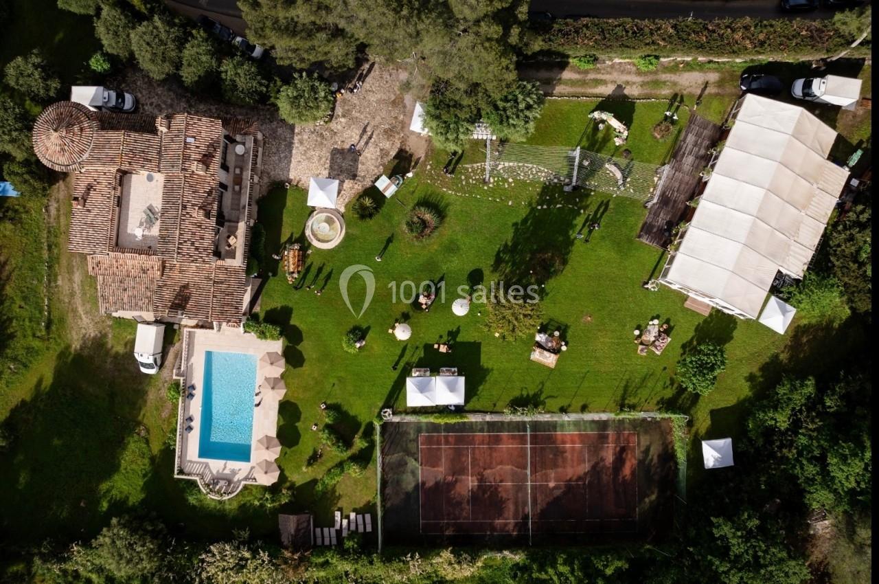 Vue aérienne d'une propriété avec piscine, court de tennis, espaces verts aménagés et structures temporaires.