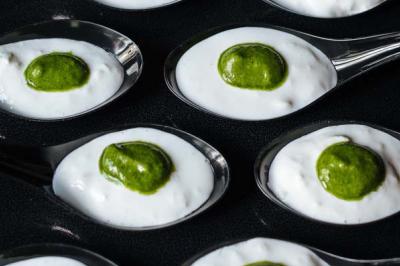 Cuillères contenant une mousse blanche garnie d'une touche de sauce verte, disposées sur une surface noire.