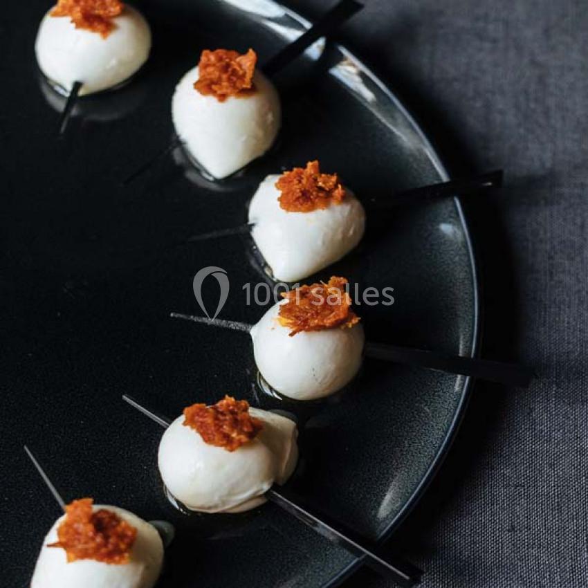 Billes de mozzarella sur des piques, garnies de chips croustillantes, disposées en cercle sur une assiette noire.